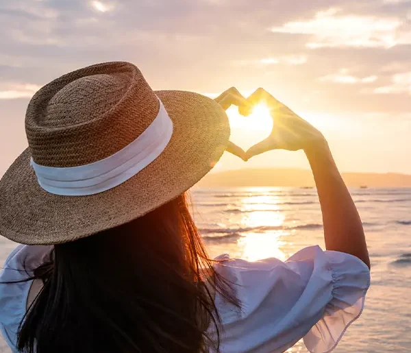 Reisende am Strand formt mit den Händen eine Herzform, zu unseren Firmen Werten.