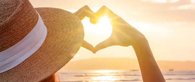 Reisende am Strand formt mit den Händen eine Herzform, zu unseren Firmen Werten.