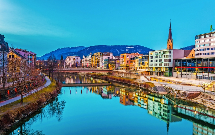 Blick auf einen Flussufer der Drau bei Sonnenuntergang in Villach, Österreich
