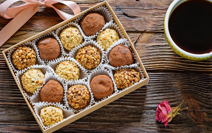 Selbst gemachte Schokoladentrüffel in Geschenk-Box, Tasse schwarzen Kaffee und trockene Rose auf Holztisch.