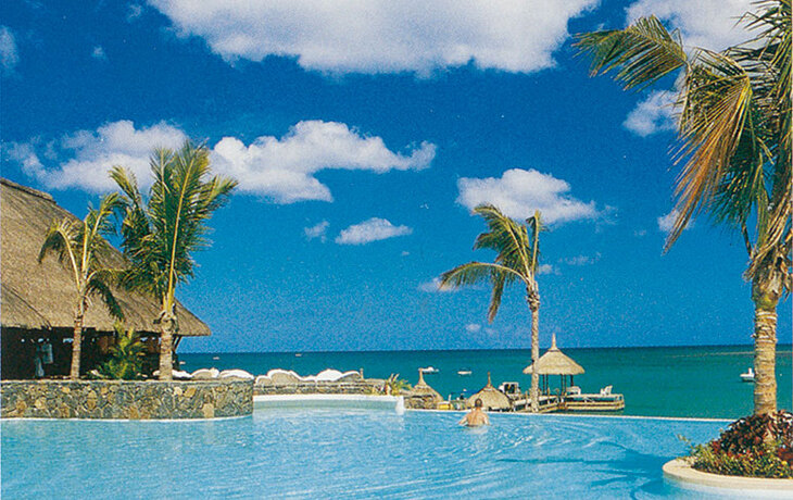 Schwimmbecken und Palmen vor einem klaren blauen Himmel und Meer im Maritim Hotel Mauritius.